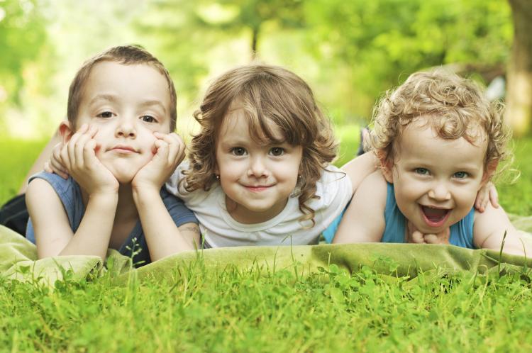 Three young children lying in the grass smiling.