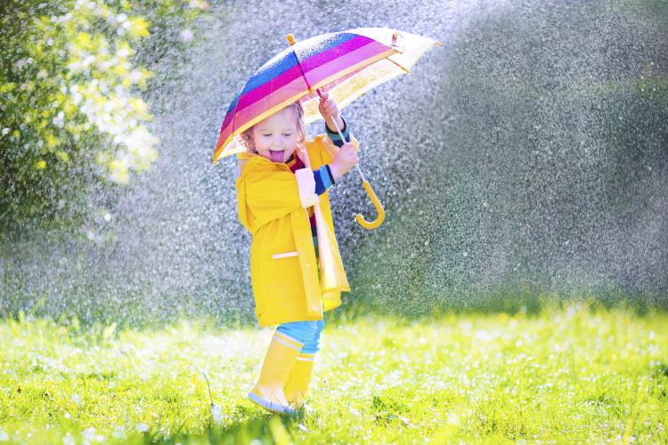 Laughing toddler with umbrella playing in the rain.
