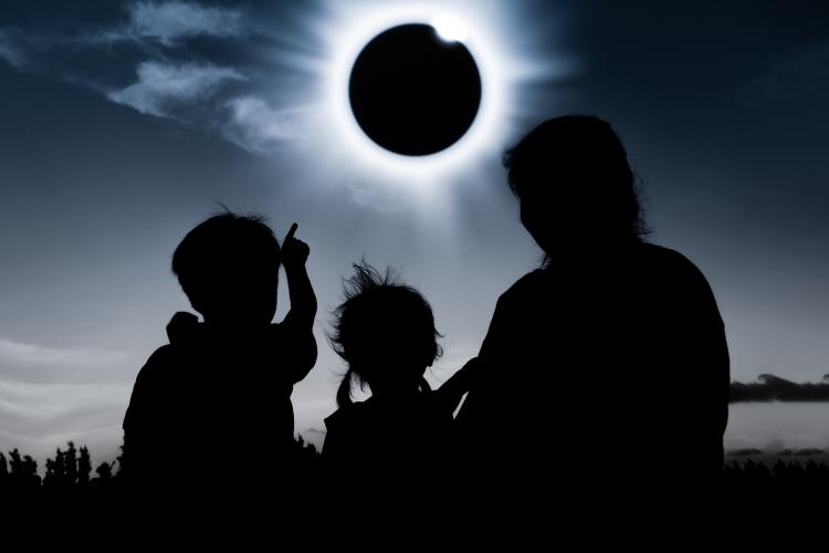 Silhouettes of two children and a woman watching the diamond ring effect on a totally eclipsed Sun.