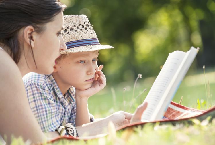 A mother reading a book with her son in a park.