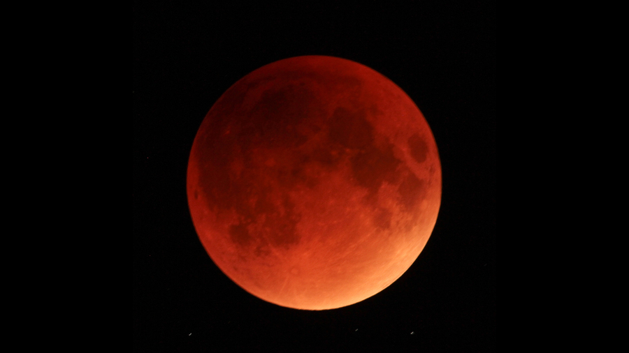 een heldere rode maan tijdens een totale maansverduistering tegen een zwarte nachtelijke hemel.