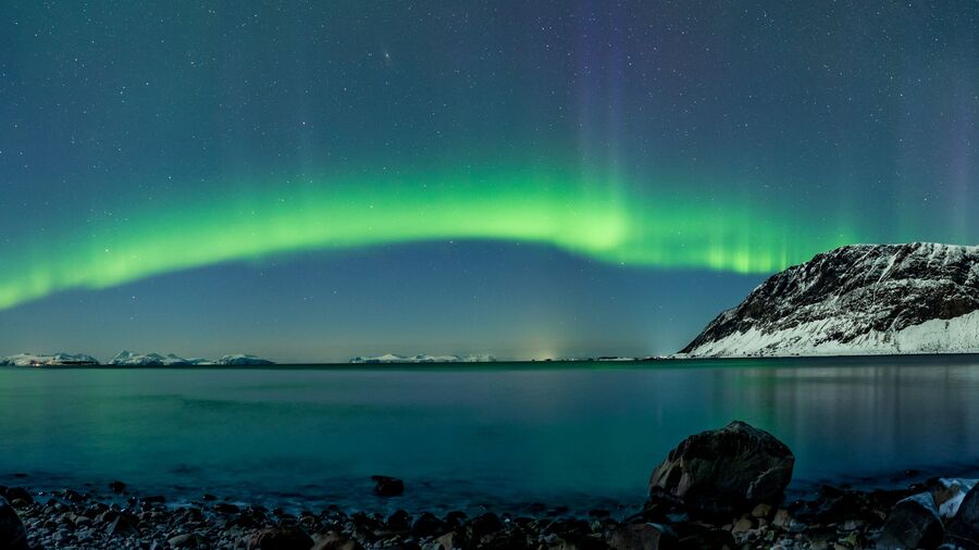 A vivid green aurora arc visible over Harstad, northern Norway.